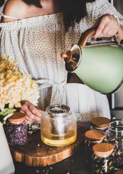Woman in rustic kitchen pouring hot water from kettle into teapot, close up
