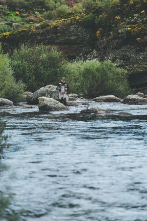 Confident man fishing with rod while standing in river stream