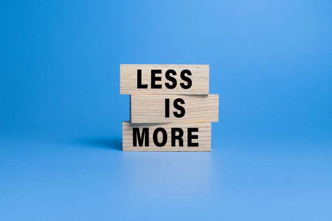 less is more words symbol on wooden block isolated on blue background. motivational quote concept