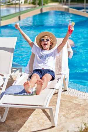 Top view boy with arms raised screaming and relaxing on lounger