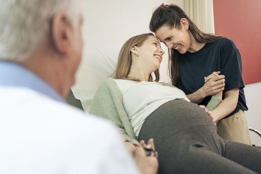 Loving lesbian couple sharing an intimate moment during a pregnancy check-up.