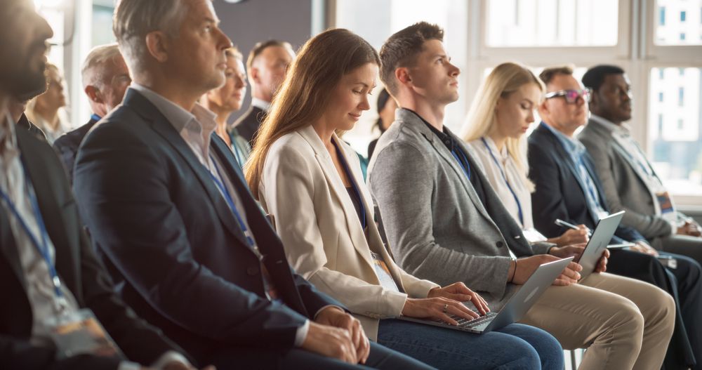 Young Woman Sitting in a Crowded Audience at a Business Conference. Female Attendee Writing Important Bullet Points on a Laptop. Keynote Speech in an Auditorium with Successful Businesspeople.