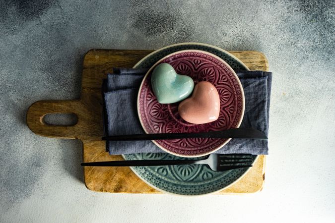 Ornate plates with pastel ceramic heart on cutting board