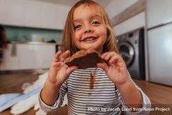 Beautiful little girl showing a chocolate she is eating with chocolate on her shirt 5qDKa0