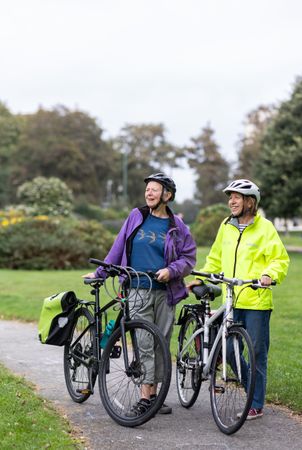 Two smiling older people standing and talking with bikes looking away