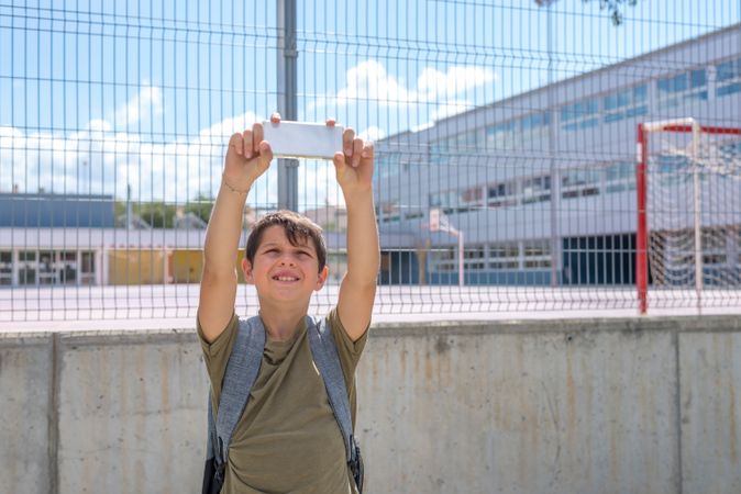 Teenage boy taking selfie in front of school fence