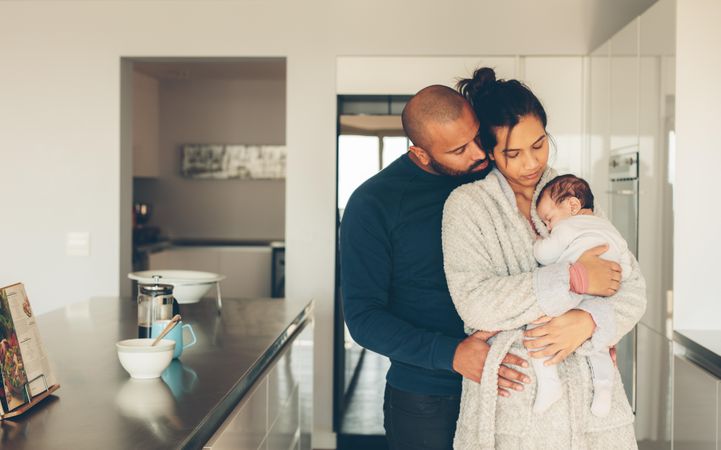 Young father and mother holding their baby boy in kitchen