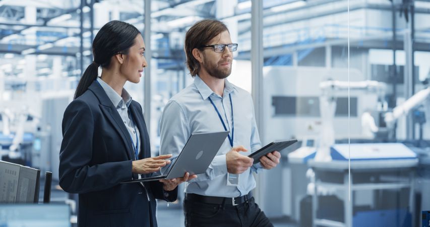 Factory Managers Using Computer Devices at Modern Manufacture with Autonomous Robot Hands. Female and Male Specialists Monitoring Technical Data, Analyzing Reports and Planning Updates