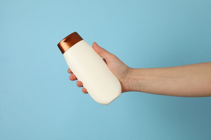 Female hand holds shampoo bottle on blue background, space for text