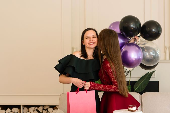 Teen girl kissing woman holding gift bag and balloons