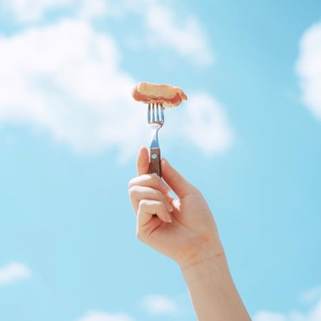 Person holding fork with food under blue sky