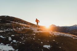 Man in red jacket walking on shrubland at sunset in Dolomites, Italy 0vKJx5