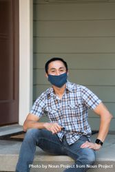 Man sitting in front of house wearing mask smiling and looking at camera 5ngXm4