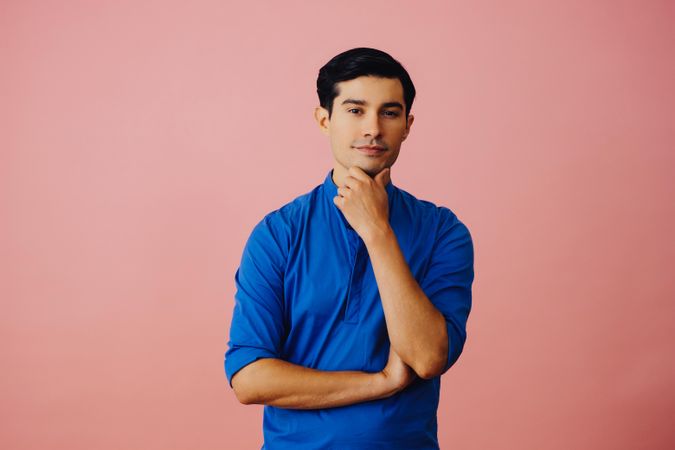 Medium shot of Latino man in pink studio with hand on chin