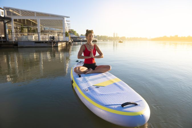 Woman peacefully meditating on paddleboard near pier