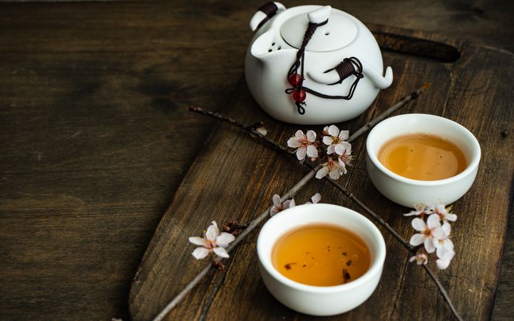 Cups of green tea and pot with floral petals with copy space