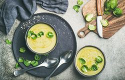 Two bowls of Brussels sprout soup, on dark plate, garnished with fresh sprouts, with wooden board
