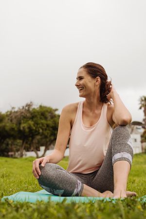 Portrait of a smiling woman sitting in park on a fitness mat