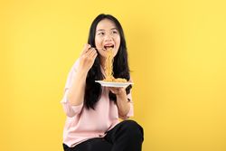 Young Asian Woman Holding A Plate of Fried Instant Noodle, Sitting on Yellow Background