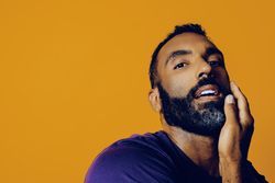 Sensual Black man in yellow studio with one hand to his face