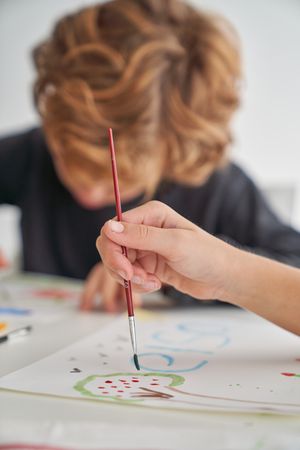 Unrecognizable kid painting near boy at table