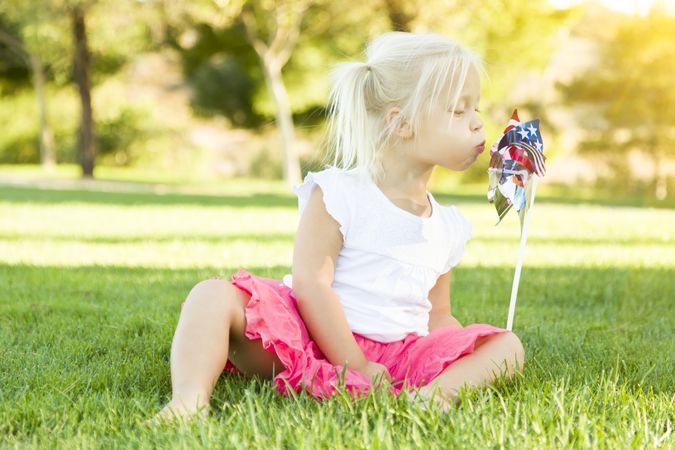 Little Girl In Grass Blowing On Pinwheel