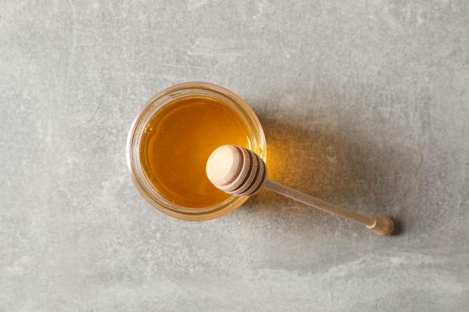 Glass jar with honey and dipper on grey background, copy space