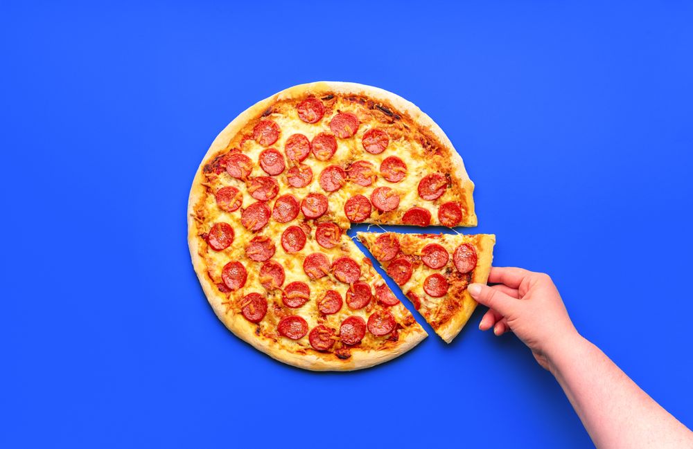 Woman's hand taking a slice of freshly baked pepperoni pizza