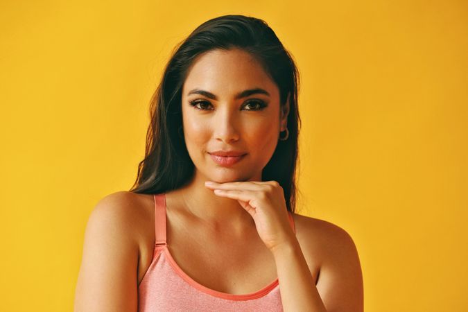 Headshot of confident Hispanic woman looking at camera with hand up to her chin in a yellow room