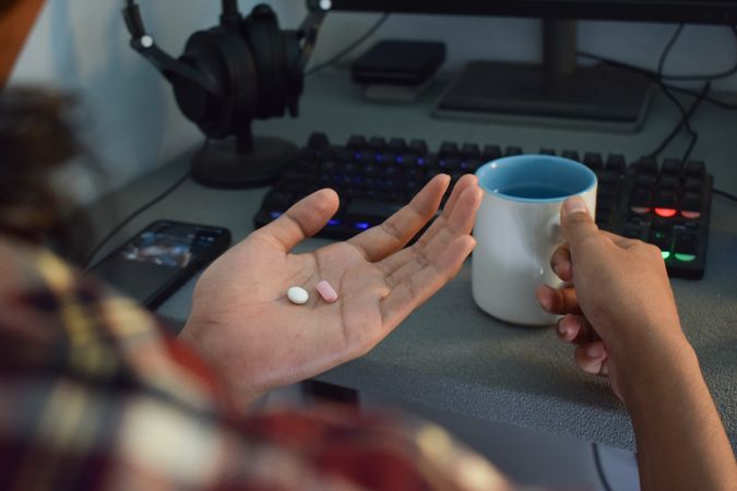 Person sitting at desk with two pills in palm of hand