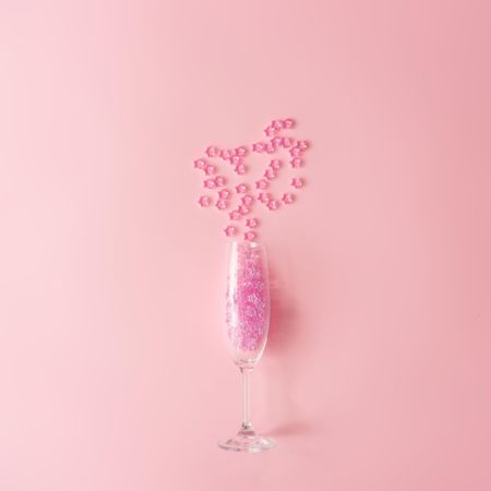 Champagne glass with pink glitter on pastel pink background