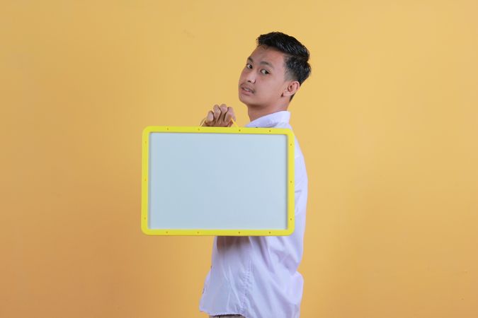 Portrait a young man in yellow backdrop holding a blank note board