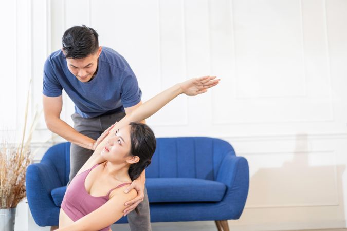 Asian man helping woman with yoga stretch