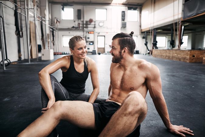 Man and woman sitting on gym floor smiling at each other
