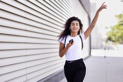 Arab woman in sport clothes with curly hair walking outside while dancing and pointing up
