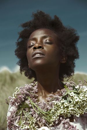 Black woman wearing floral wreath around her neck closing her eyes