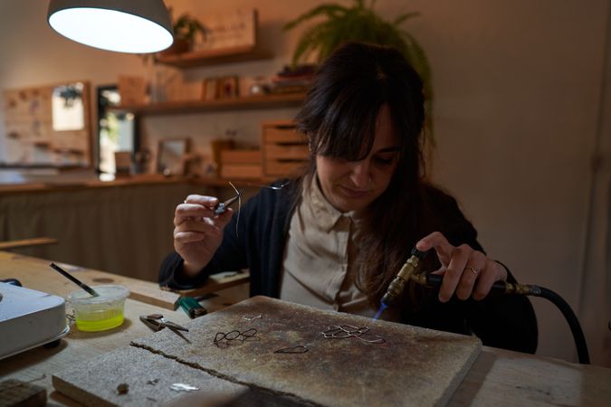 Concentrated craftswoman using soldering torch during jewelry maker