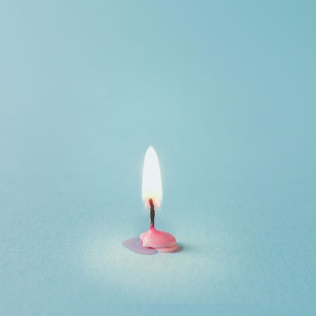 Lit pink candle on blue background