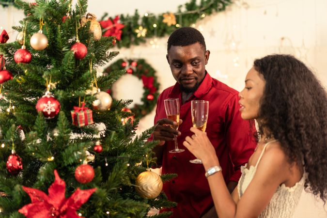 A Black couple toasting with champagne glasses at decorated Christmas tree