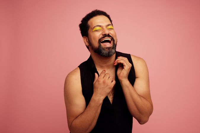 Drag queen with eye makeup smiling on pink background with his eyes closed