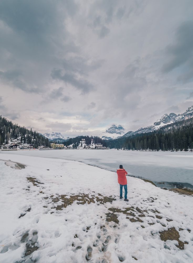 Unrecognizable person standing in snow surrounded by forest and mountains