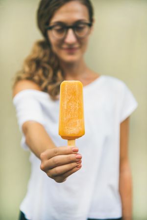Woman in t-shirt and glasses holding orange popsicle