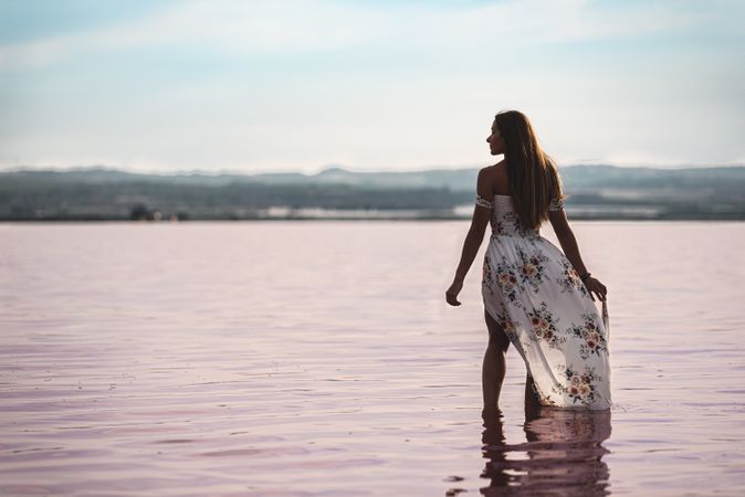 Peaceful woman in white dress walking ankle deep in pink lake