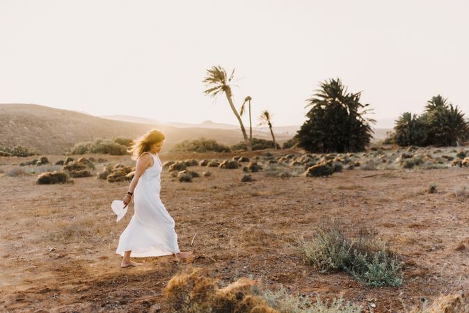 Woman in white dress in dry field in sunlight