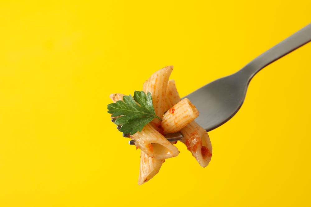 Fork with tasty pasta on yellow background, close up