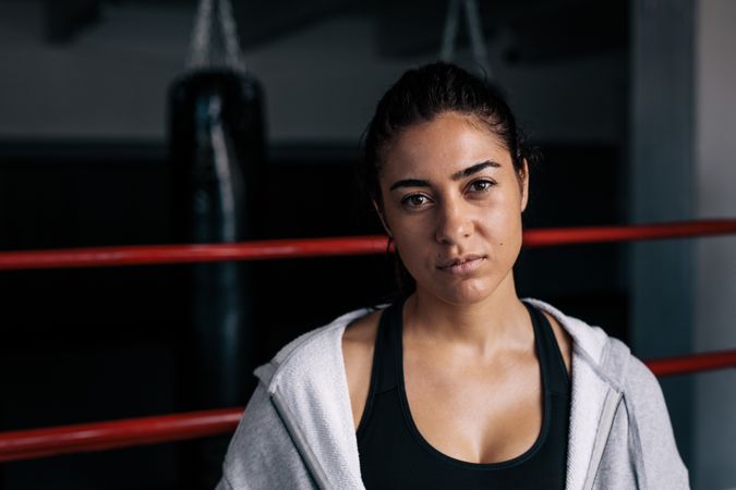 Portrait of serious female boxer standing in the ring in hoodie