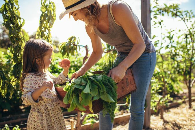 Mother and daughter with freshly harvested vegetables in garden