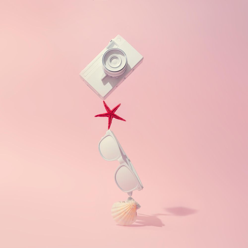 Camera, sunglasses and sea shells on pastel pink background