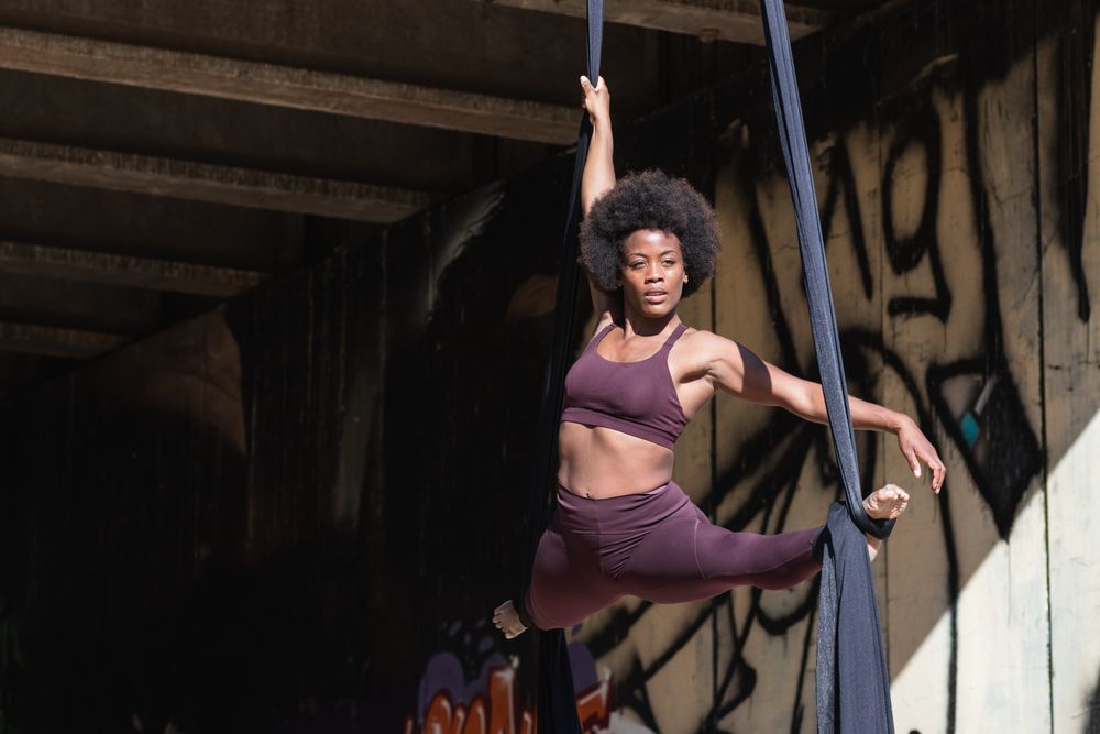 Slim woman doing yoga with aerial silks in city