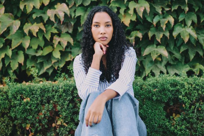 A contemplative young woman sitting quietly amidst the vibrant greenery surrounding her